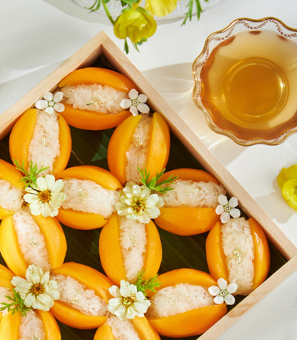 Wooden box of mango sticky rice servings with gold leaf and fresh flowers, Thai tropical dessert gift
