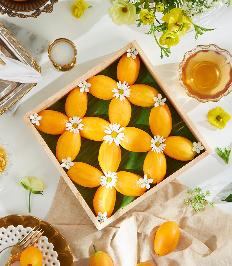 Premium yellow tropical fruits arranged on banana leaf with fresh white daisies and gold accents, artisan gift presentation