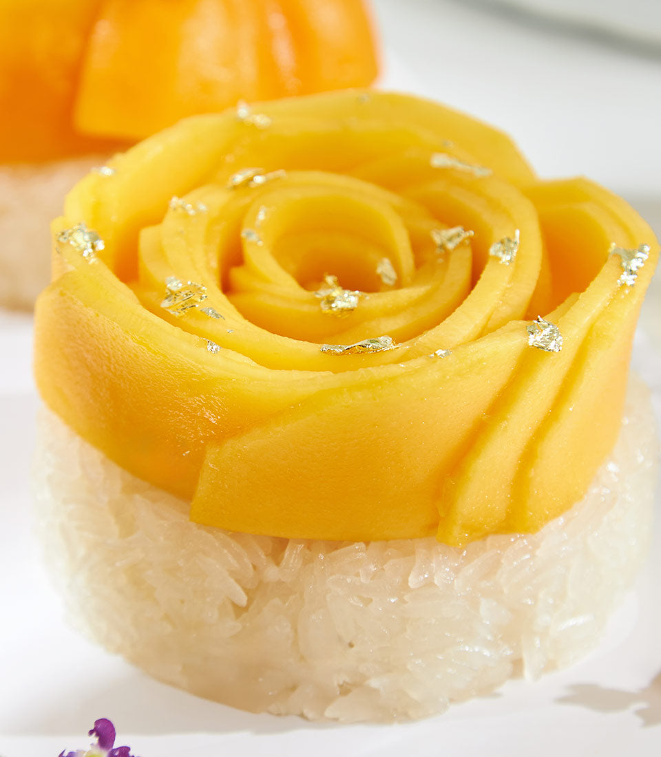 Mango sticky rice dessert with edible gold leaf and tropical fruit rose presentation