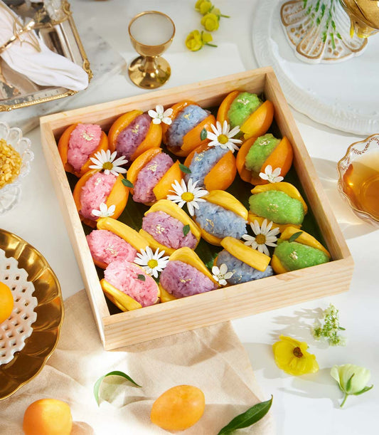 Exotic tropical fruit sticky rice desserts in rainbow colors with edible flowers and gold leaf in wooden gift box