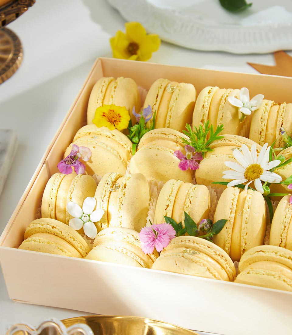 Golden mango macarons with fresh flowers and gold leaf in luxury gift box