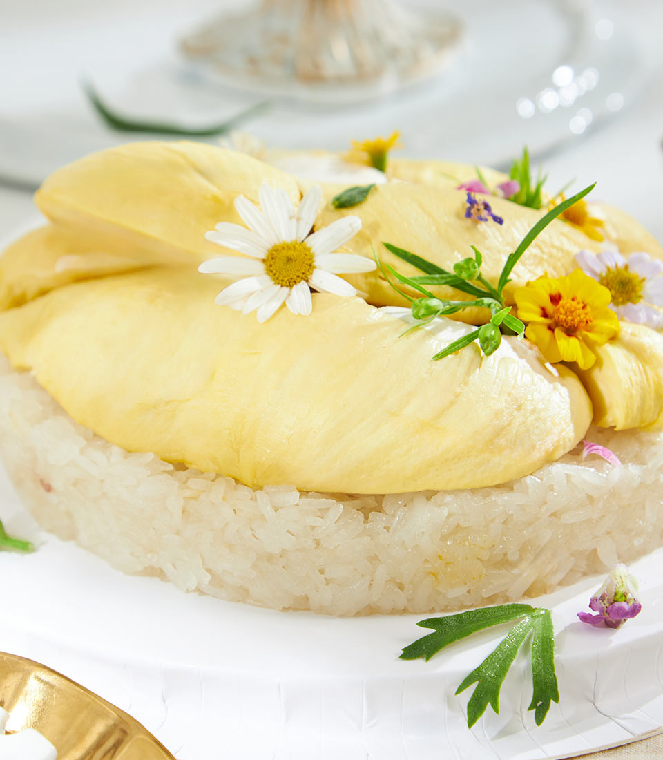 Mon Thong durian with sticky rice dessert, vibrant yellow fruit on white rice bed with fresh flower garnish