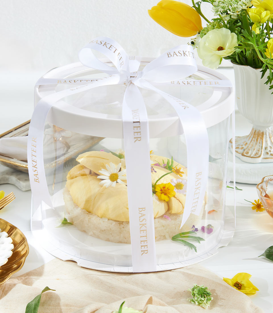 Golden durian and sticky rice dessert in elegant gift box with edible flowers and white satin ribbon