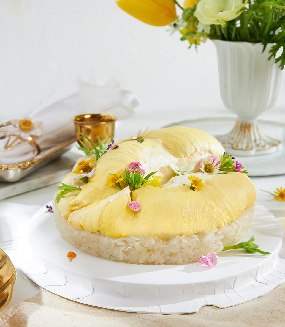 Pale golden durian with sticky rice dessert, edible flowers, elegant plated presentation for tropical gifting