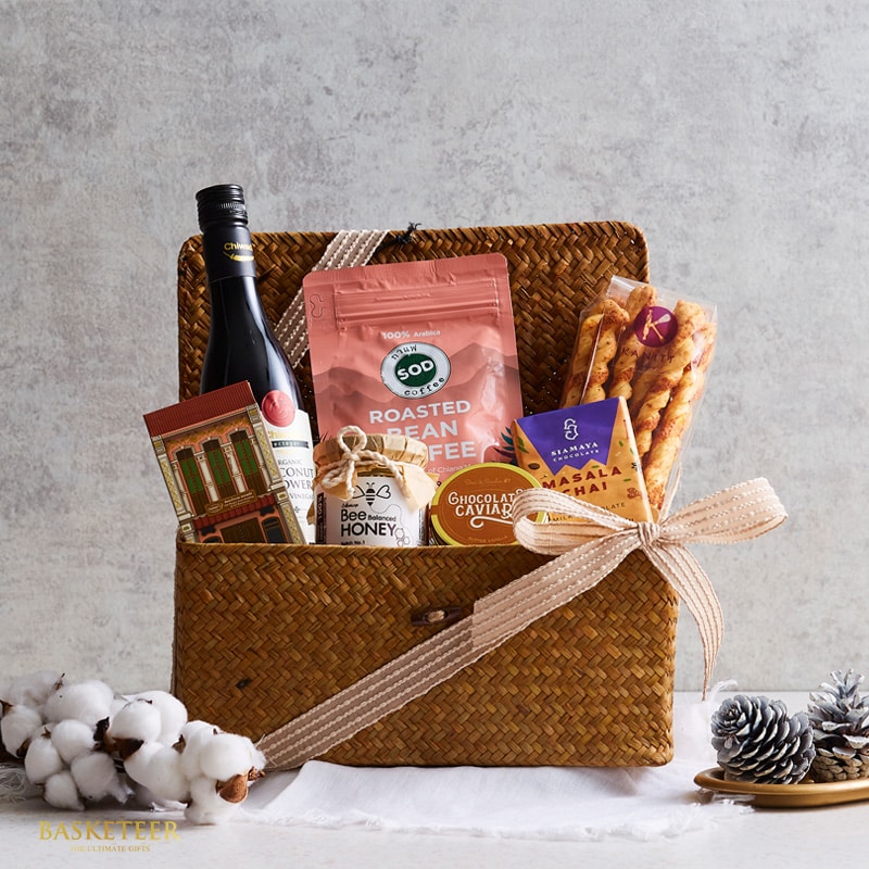 Woven straw gift basket with wine, gourmet coffee, honey, chocolate, and chai tea on textured background