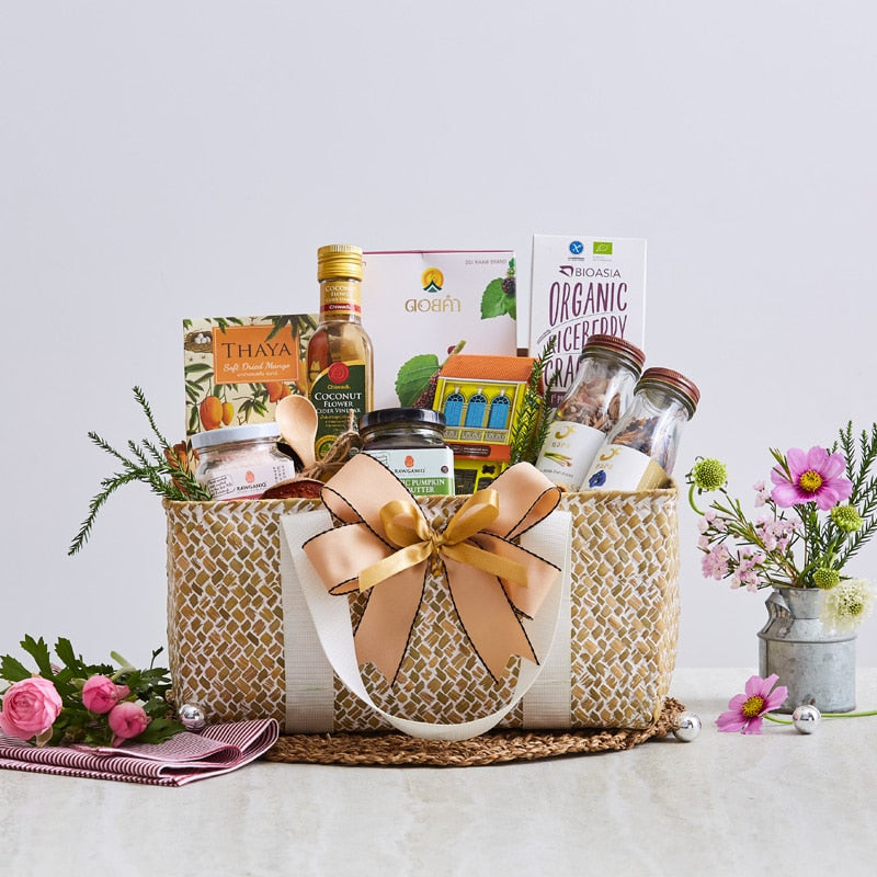 Woven straw gift basket with peach ribbon bow filled with gourmet goods, coconut flower syrup, pumpkin butter, dried mango,