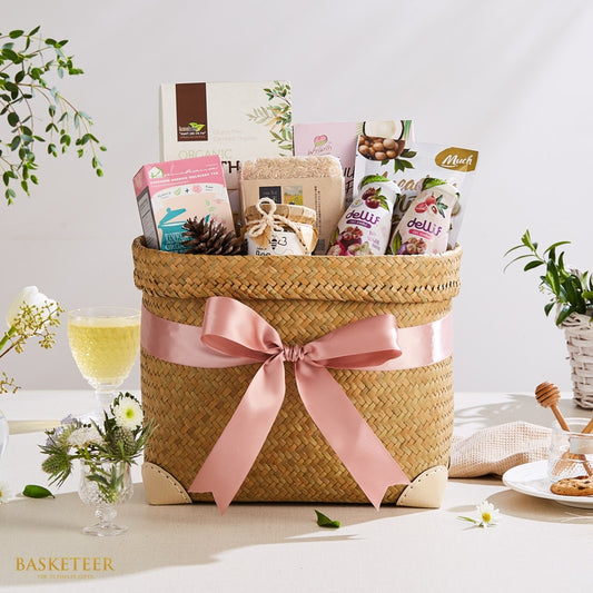 Premium Thai gift basket with organic tea, honey, dried fruit, and artisan treats in woven straw with pink bow