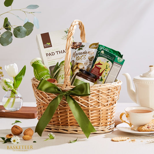 Wicker gift basket with green ribbon filled with organic pad thai, macadamia nuts, jasmine rice, mulberry tea, and gourmet