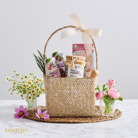 Woven rattan gift basket with honey, gourmet beverages, tea, and fresh daisies and peonies