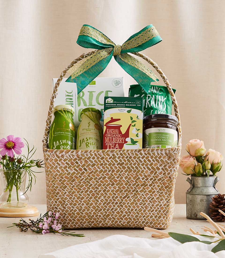 Woven natural fiber gift basket with organic jasmine rice, mulberry tea, coconut flower nectar, and grains, tied with green