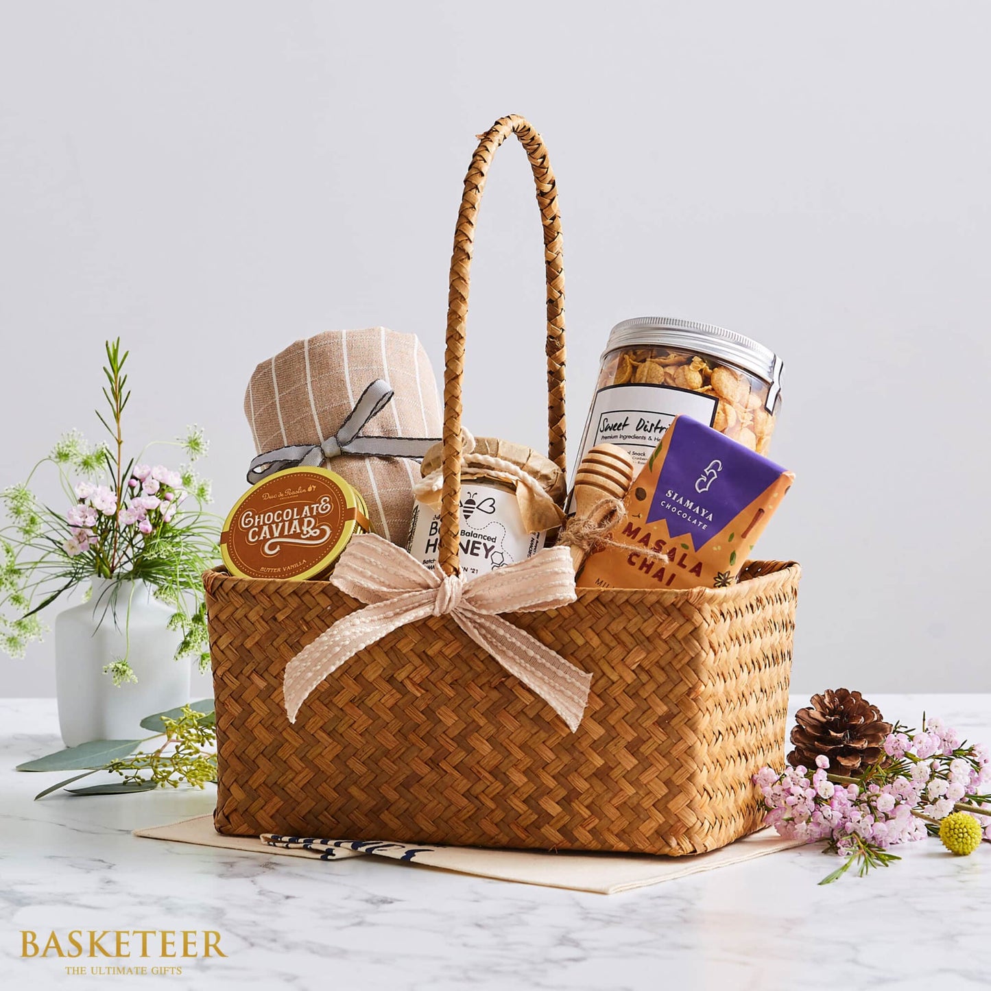 Woven straw gift basket with pink ribbon bow filled with gourmet bakery items, honey, chocolate, and artisan treats