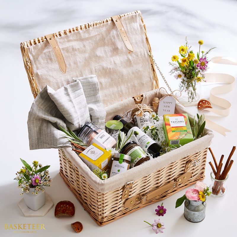 Light wicker hamper with gourmet goods, honey, olive oil, tea, and fresh flowers for premium gifting