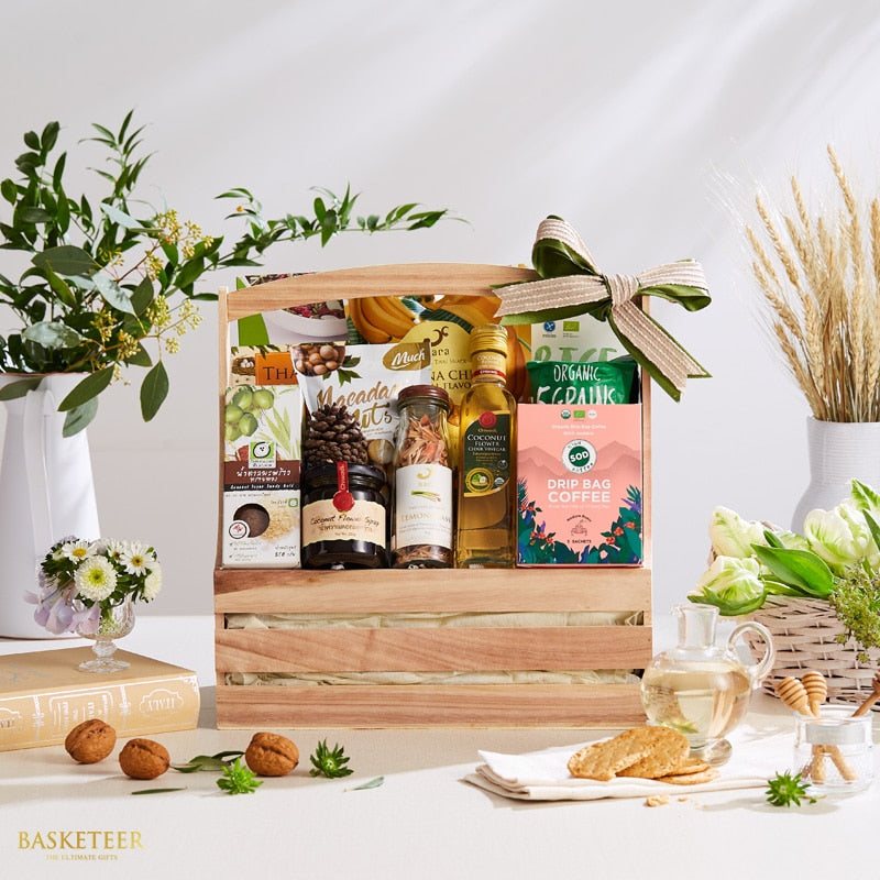 Wooden gift crate with Thai gourmet foods, macadamia nuts, coconut oil, coffee, and spices tied with striped ribbon