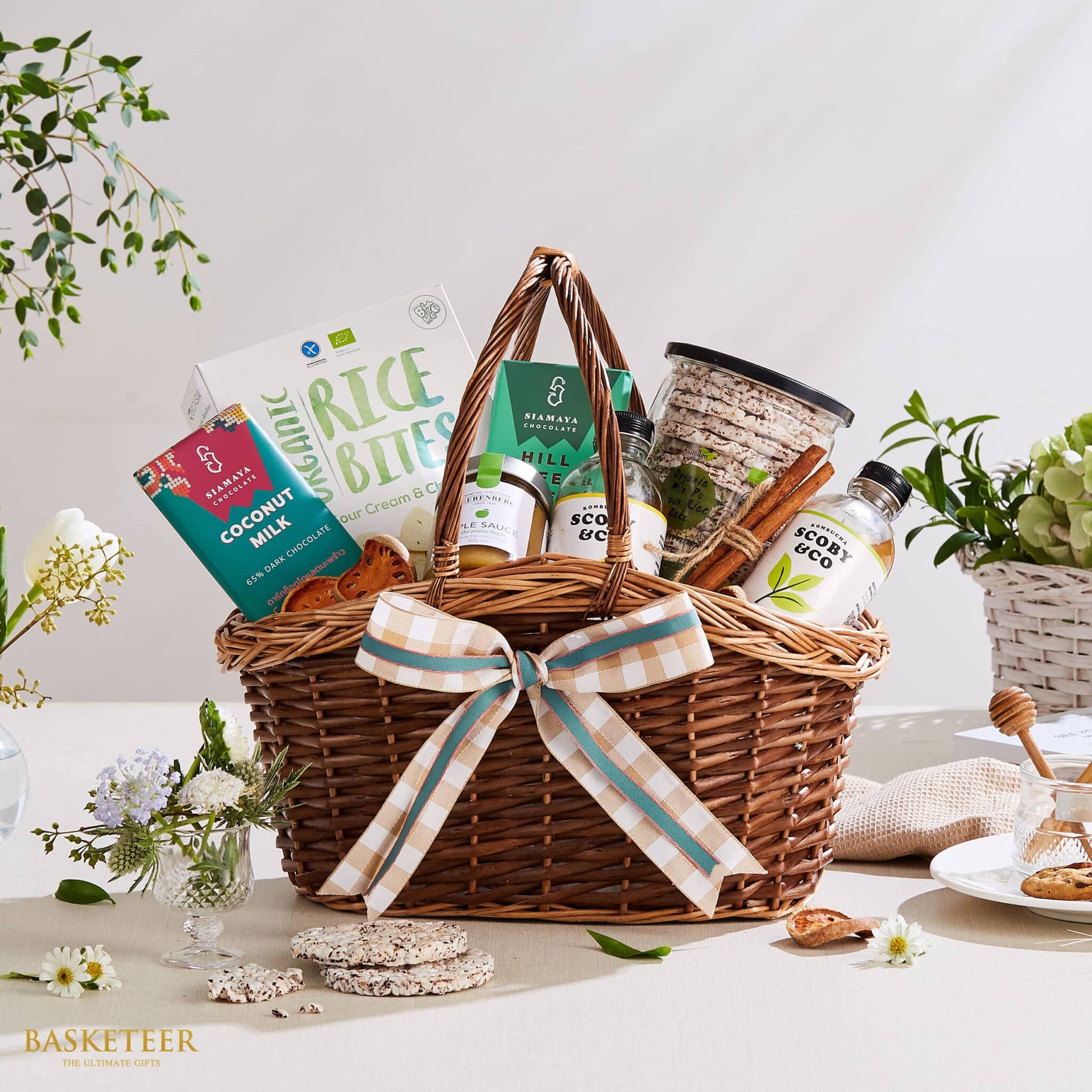 Woven wicker gift basket with organic Thai gourmet treats, coconut chocolate, kombucha, and rice cakes tied with cinnamon,