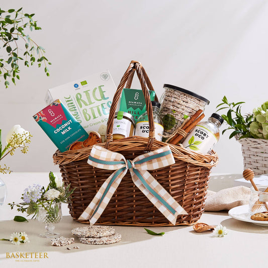 Woven wicker gift basket with organic Thai gourmet treats, coconut chocolate, kombucha, and rice cakes tied with cinnamon,