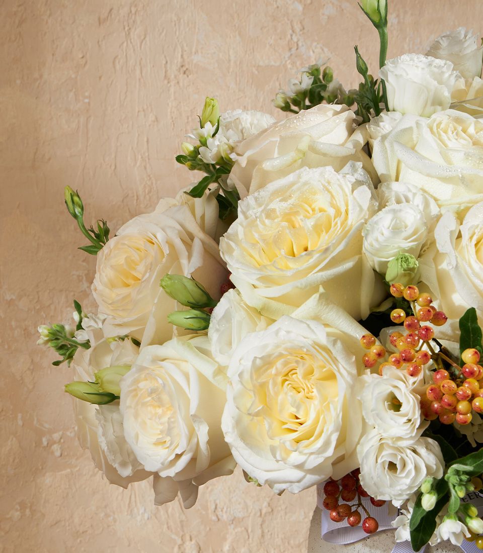 Fresh white roses and cream blooms with orange berries in elegant vase arrangement