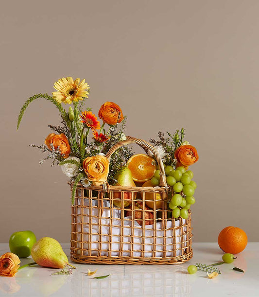 Wicker basket birthday gift with fresh fruits, orange ranunculus, and yellow gerbera daisies