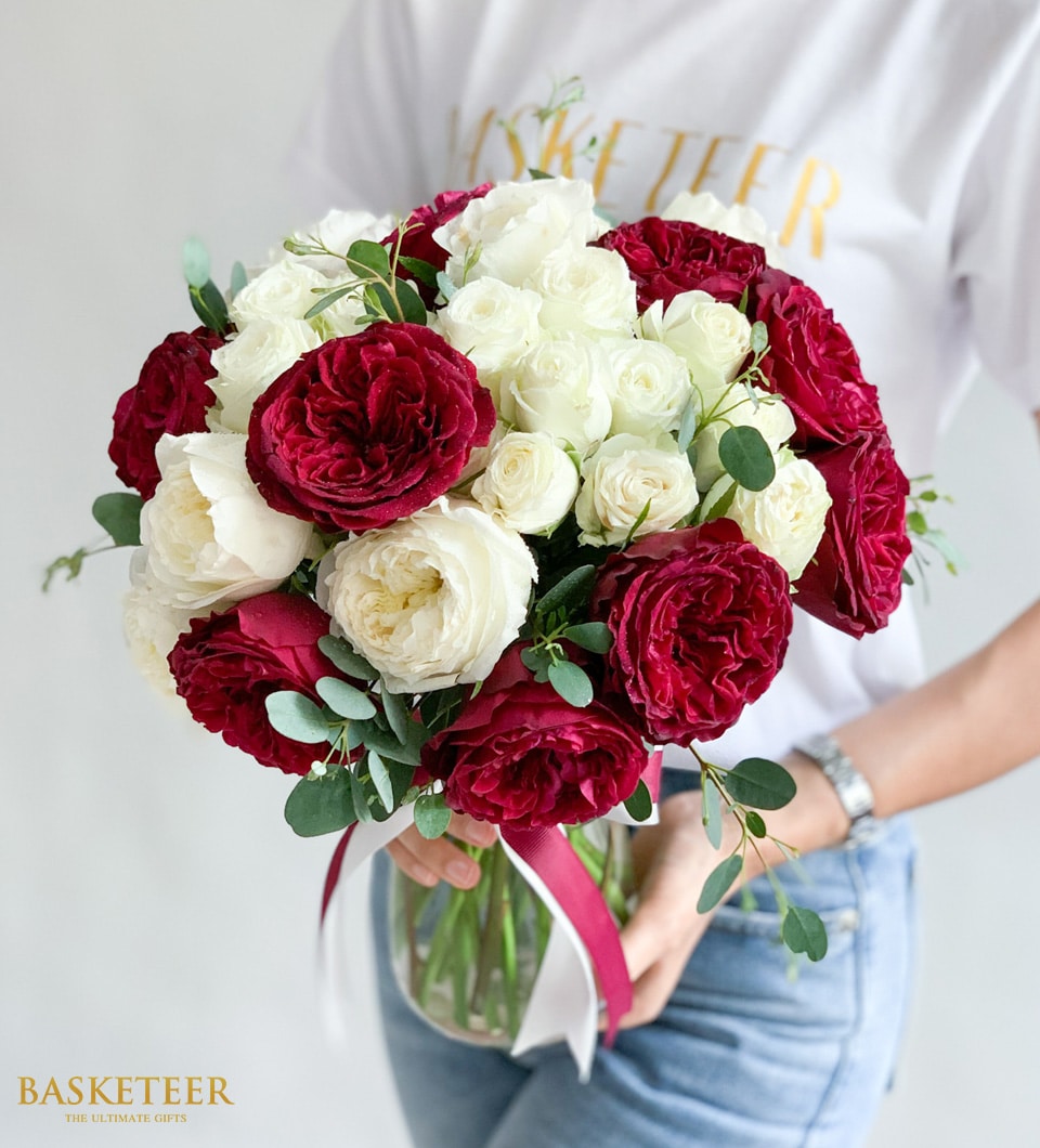 Vibrant red and white rose bouquet in clear glass vase with eucalyptus, tied with burgundy ribbon
