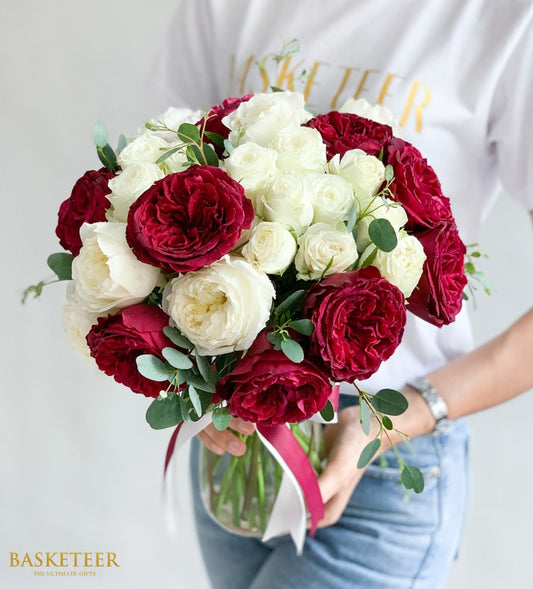 Vibrant red and white rose bouquet in clear glass vase with eucalyptus, tied with burgundy ribbon