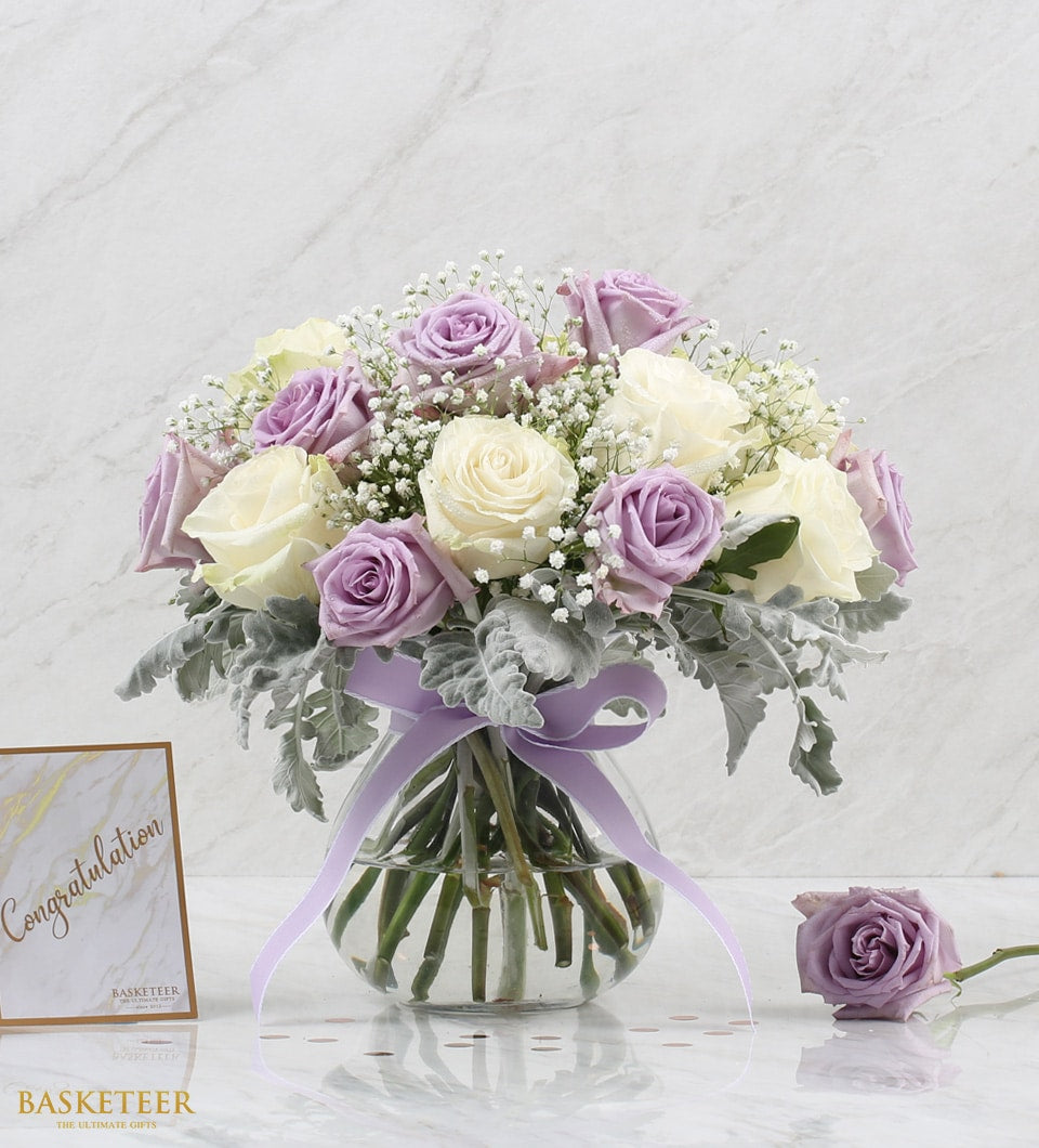 Purple and cream roses with baby's breath in clear glass vase, tied with lavender ribbon