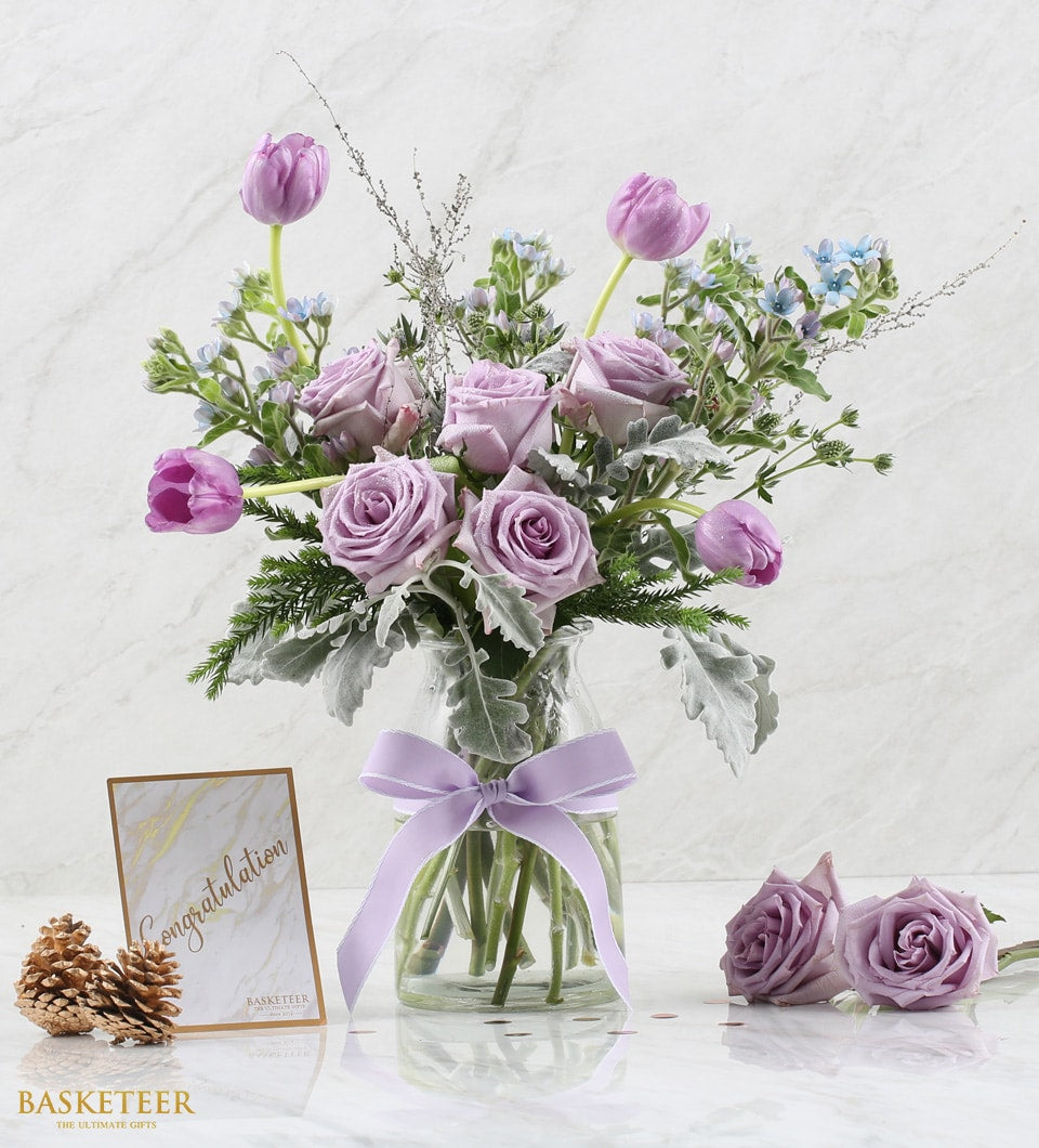 Purple roses and tulips in clear glass vase with congratulations card and rose gold confetti