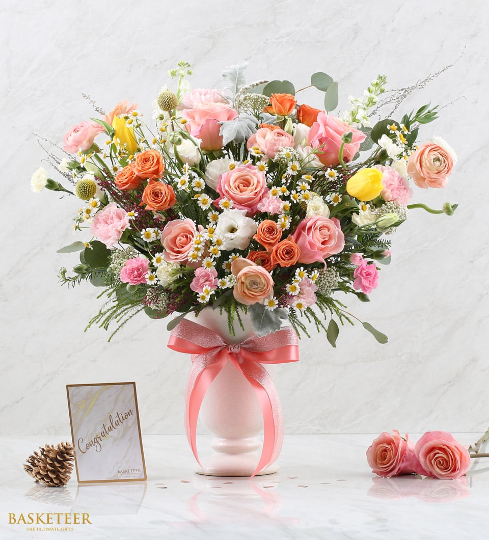 Vibrant pink, orange, and yellow mixed flower arrangement in light pink vase with coral ribbon bow, congratulations card,