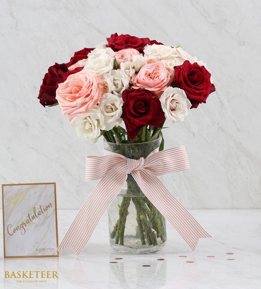 Fresh roses bouquet in clear glass vase with pink and white ribbon, mixed red and blush blooms