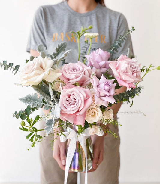 Fresh lavender and pink roses with eucalyptus in clear glass vase, water droplets on petals