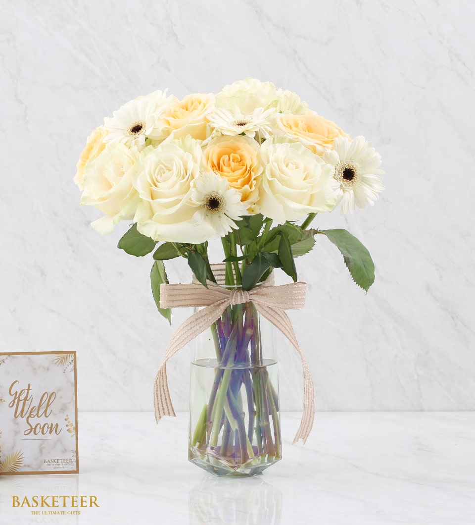 White roses and gerbera daisies in glass vase with beige ribbon