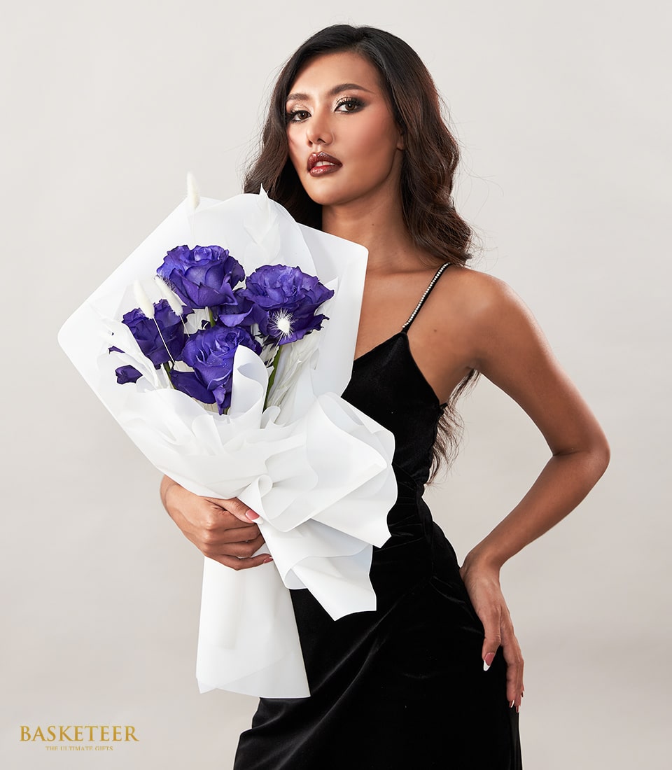 Deep purple Eustoma bouquet with dried botanicals in white tissue wrap, held by woman in black velvet dress