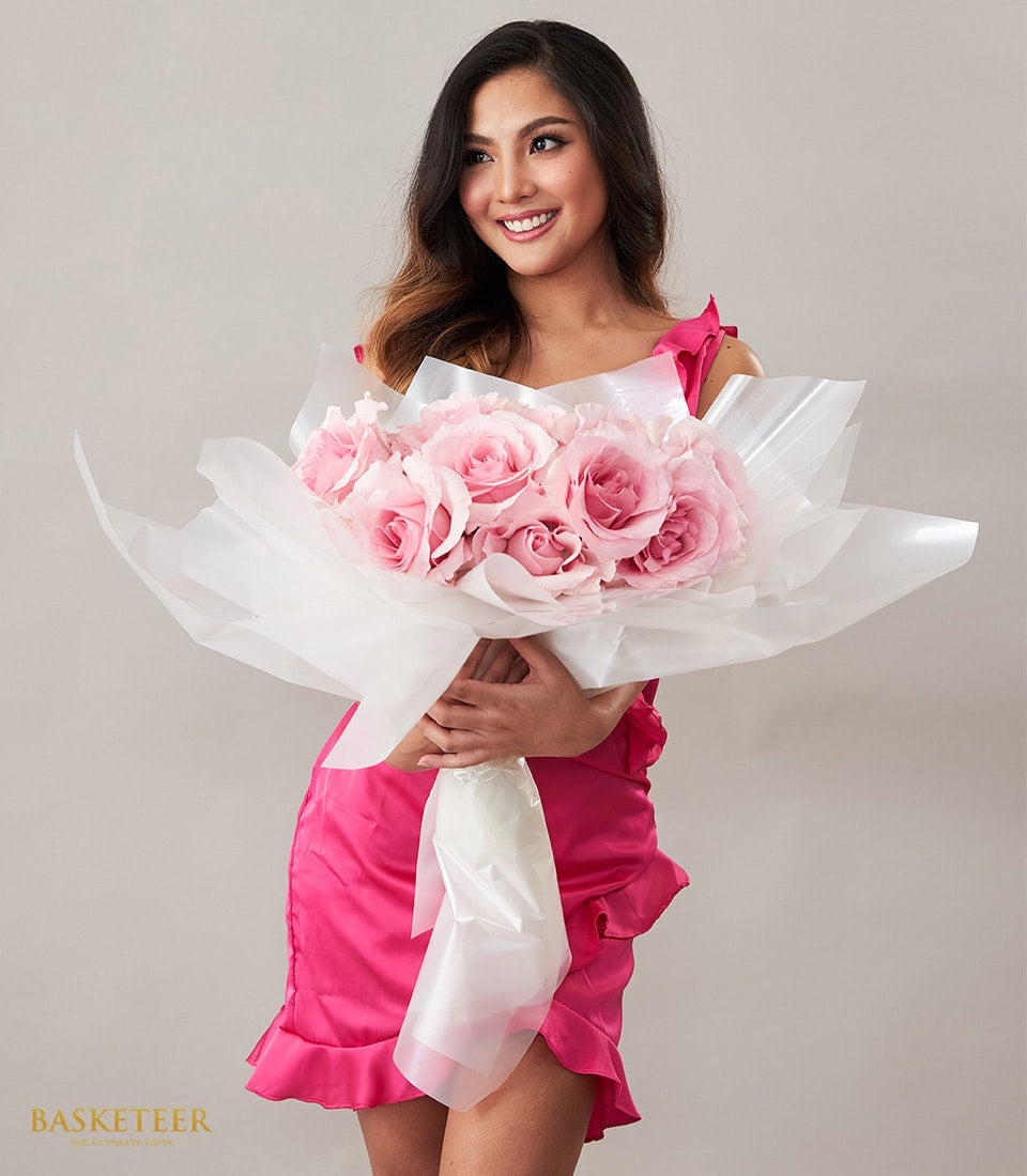 Woman in fuchsia dress holding large bouquet of light pink roses wrapped in white paper