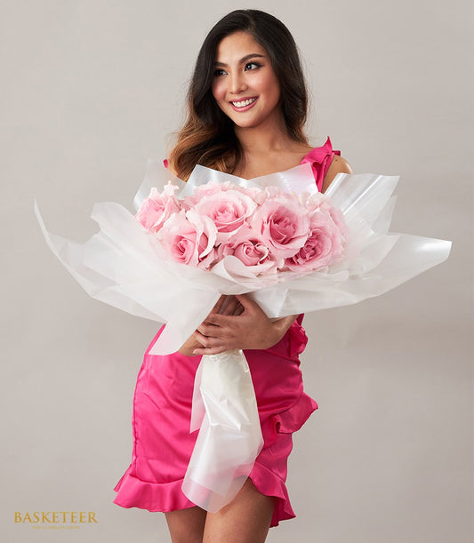 Woman in fuchsia dress holding large bouquet of light pink roses wrapped in white paper