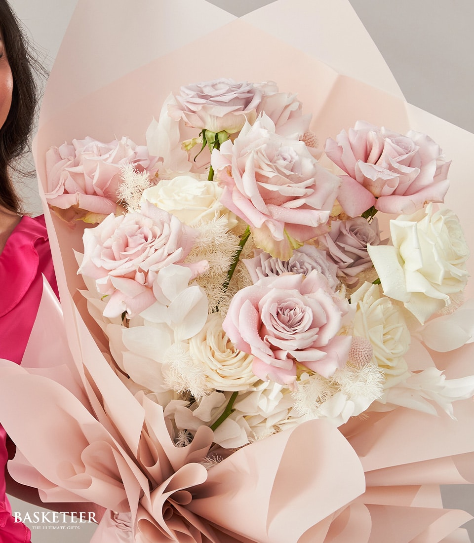 Pure of Love roses bouquet in pale pink, lavender, and cream with white filler flowers, wrapped in blush paper for