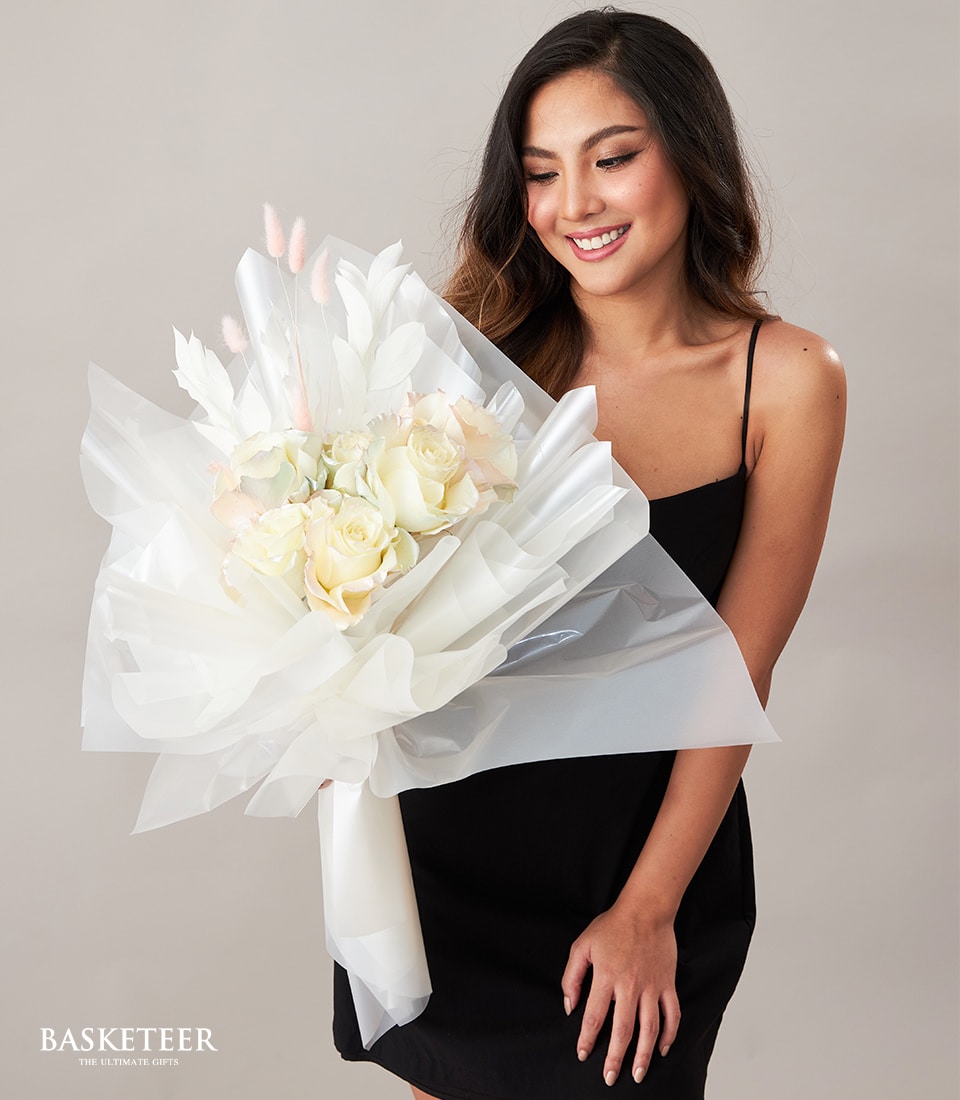 White and pale yellow rose bouquet with dried foliage, wrapped in translucent paper and tied with ribbon, Valentine's Day