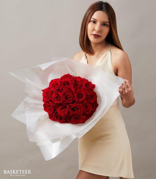 Luxe red rose bouquet wrapped in white paper with satin ribbon, held by woman in beige dress for anniversary