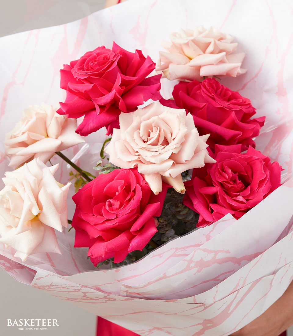 Vibrant fuchsia and cream roses bouquet wrapped in patterned white paper for anniversary