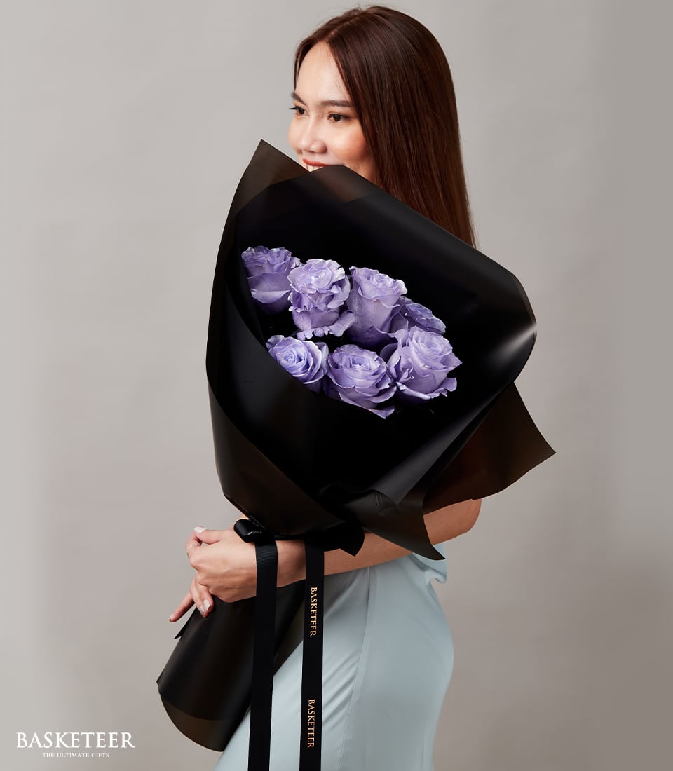 Lavender roses graduation bouquet with black ribbon, held by woman in light blue dress