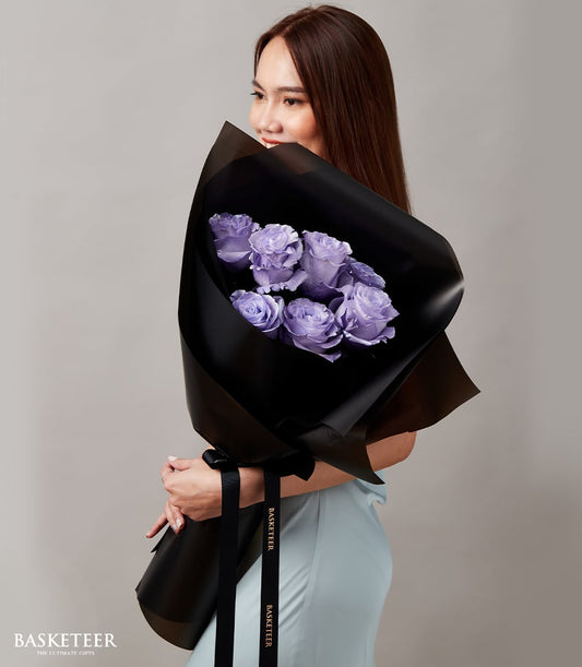 Lavender roses graduation bouquet with black ribbon, held by woman in light blue dress