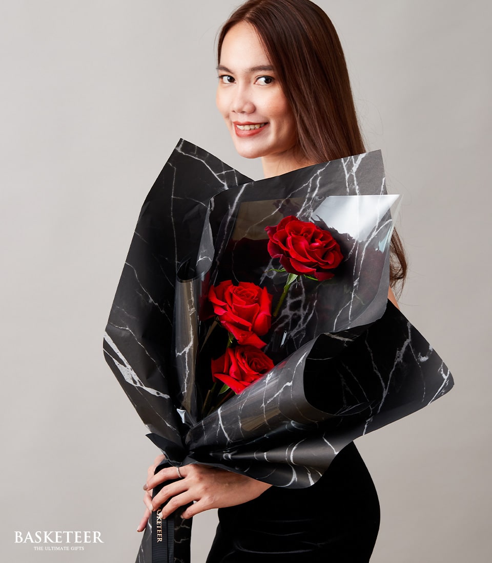 Young woman holding premium red roses bouquet with black marble wrap and black ribbon