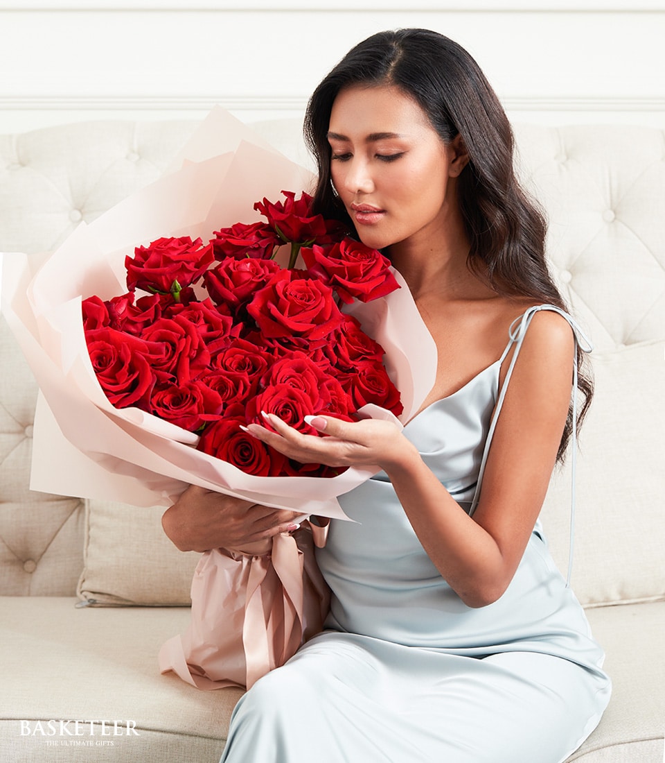 Red rose bouquet in pink paper held by woman on sofa, romantic anniversary gift