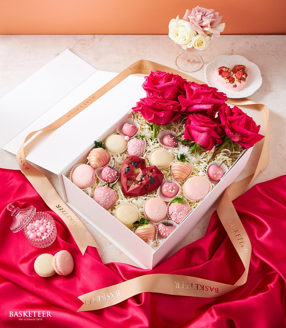Luxury Valentine's gift set with deep pink roses, chocolate-dipped strawberries, macarons, and heart-shaped red velvet cake