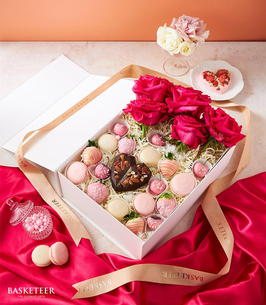 Luxury Valentine's gift box with deep pink roses, chocolate-dipped strawberries, macarons, and heart-shaped chocolates on