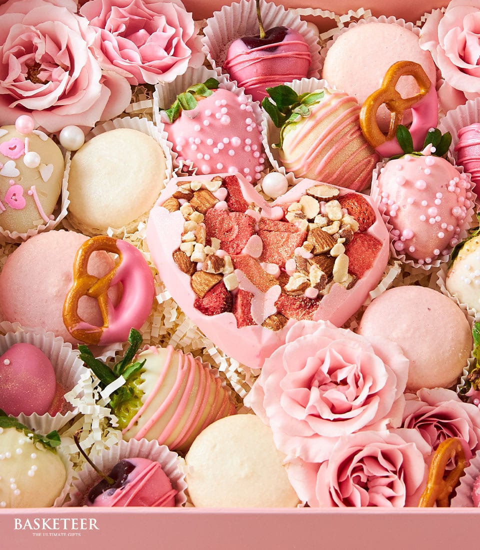 Pink gift box with chocolate strawberries, macarons, heart chocolate, cake pops, and fresh roses for birthdays or