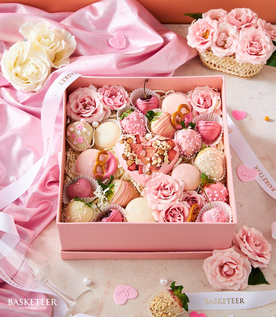 Pink chocolate and treat gift box with strawberries, macarons, and heart-shaped chocolate, tied with white ribbon