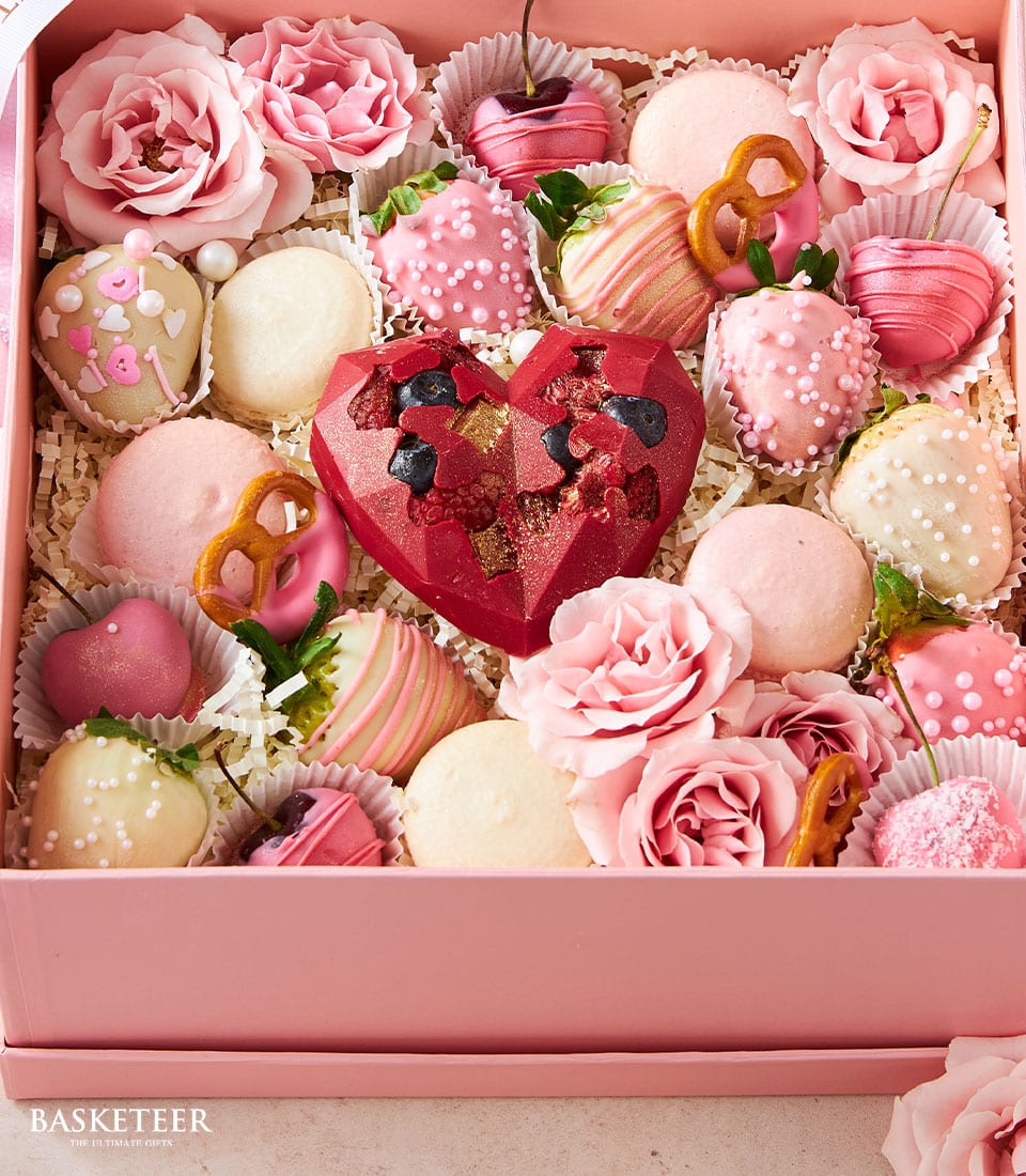 Pink luxury valentine gift box with chocolate-covered strawberries, macarons, heart truffles, and fresh roses