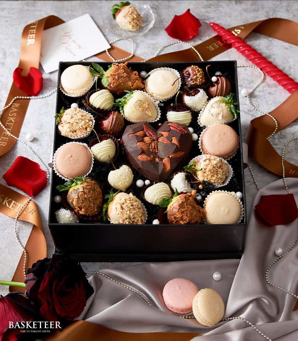 Luxury Valentine gift box with chocolate-dipped strawberries, macarons, and heart-shaped chocolate surrounded by red roses