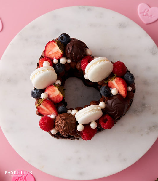 Heart-shaped chocolate cake with fresh berries, macarons, and truffles on marble board, birthday gift add-on