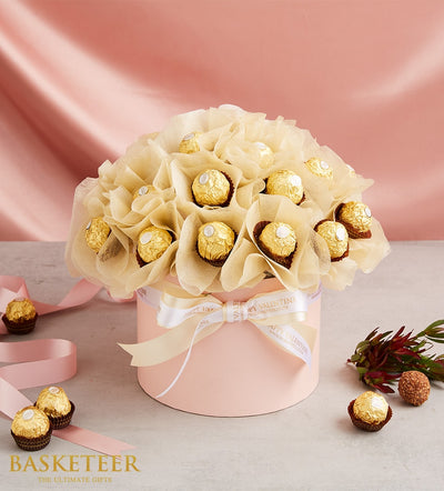 Gold-wrapped Ferrero Rocher chocolates in pink gift box with cream tissue, Valentine's Day ribbon, and romantic foliage