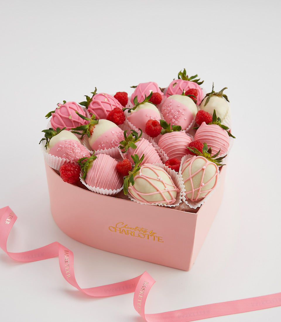 Heart-shaped box of chocolate-covered strawberries and raspberries in pink and white chocolate with decorative drizzles