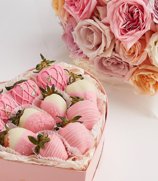 Heart-shaped box of chocolate-covered strawberries with gold leaf and rose bouquet for Valentine's Day